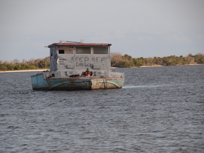 [A grey bi-level boat with the words 'Keep Off Danger' spray-painted in black on the side facing the mound.]